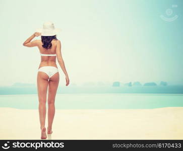 people, fashion, swimwear, summer beach and beauty concept - young woman in white bikini swimsuit from back over infinity pool at beach resort