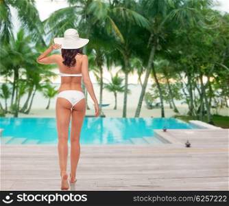 people, fashion, swimwear, summer beach and beauty concept - young woman in white bikini swimsuit from back over swimming pool at beach resort