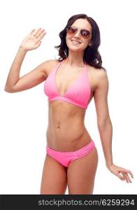 people, fashion, swimwear, summer beach and gesture concept - happy young woman in sunglasses and pink swimsuit waving hand
