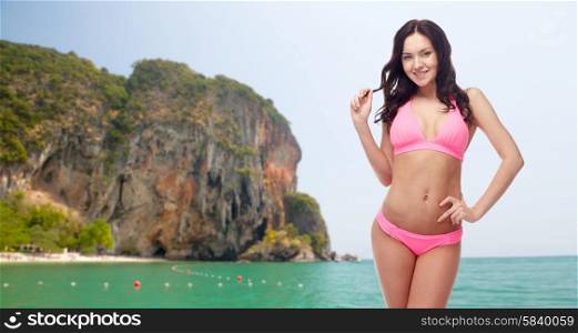 people, fashion, swimwear, summer beach and sexual concept - happy young woman posing in pink bikini swimsuit over sea and rock background