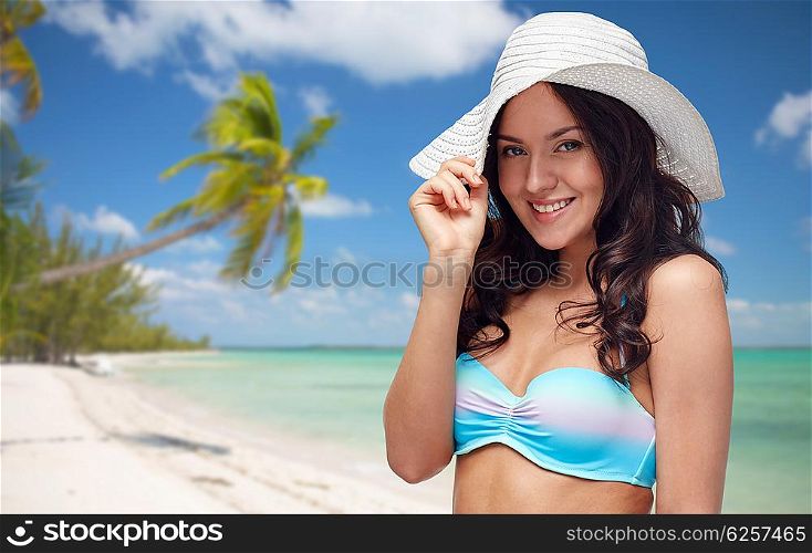 people, fashion, tourism, travel and summer concept - happy young woman in bikini swimsuit and sun hat over tropical beach background