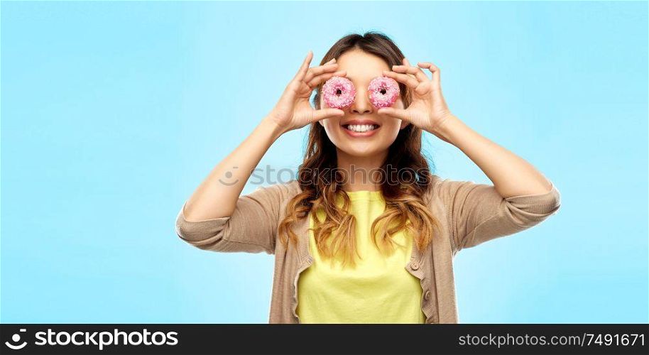 people, fast food and fun concept - happy asian young woman with donuts instead of eyes over blue background. happy asian woman with eyes of donuts