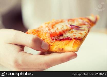 people, fast food, italian kitchen and eating concept - close up of hand holding pizza slice