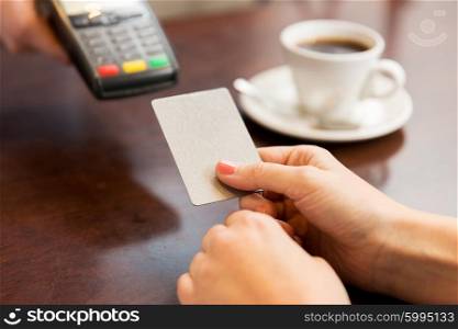 people, finance, technology and consumerism concept - close up of waitress holding credit card reader and customer hand entering pin code at cafe