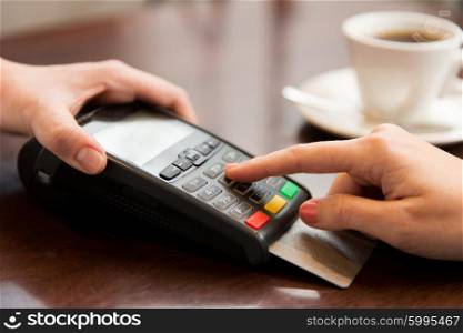people, finance, technology and consumerism concept - close up of waitress holding credit card reader and customer hand entering pin code at cafe
