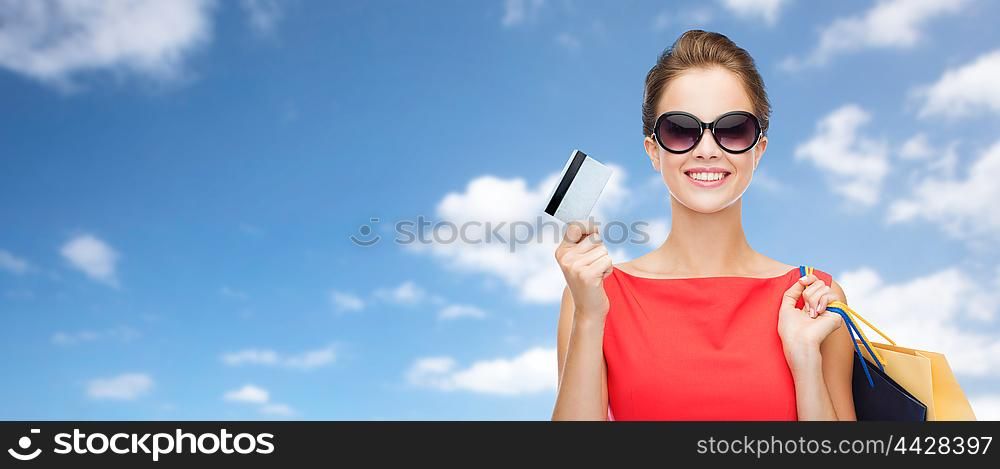 people, finances and sale concept - young happy woman with shopping bags and credit card over blue sky and clouds background