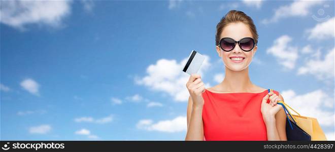people, finances and sale concept - young happy woman with shopping bags and credit card over blue sky and clouds background