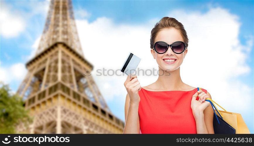 people, finances, tourism, travel and sale concept - young happy woman with shopping bags and credit card over paris eiffel tower background