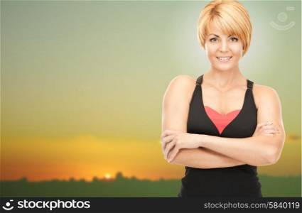 people, fitness and sport concept - happy woman posing outdoors over sunset skyline background