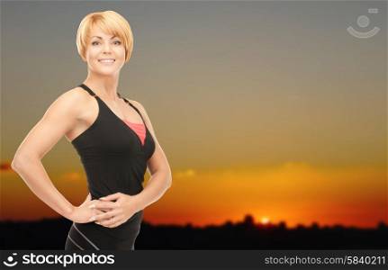 people, fitness and sport concept - happy woman posing outdoors over sunset skyline background