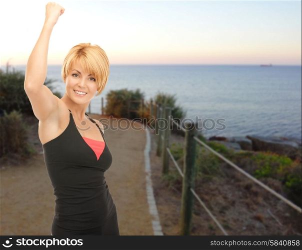 people, fitness, gesture, success and sport concept - happy woman with raised hand outdoors over beach sunset background