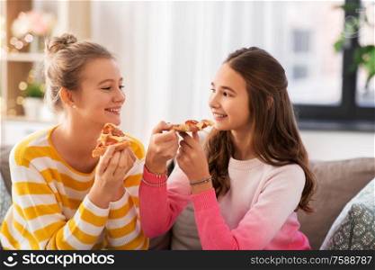 people, food and friendship concept - happy teenage girls eating pizza at home. happy teenage girls eating pizza at home