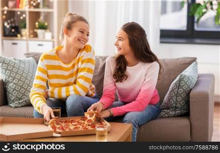 people, food and friendship concept - happy teenage girls eating takeaway pizza at home. happy teenage girls eating takeaway pizza at home