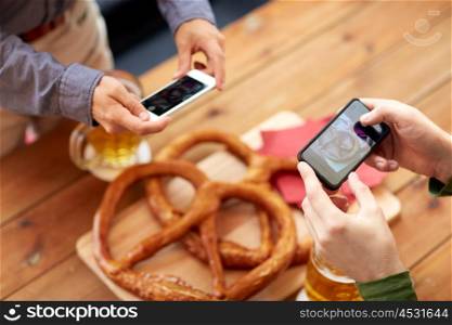 people, food, and technology concept - close up of hands with smartphone picturing beer and pretzel at bar or pub