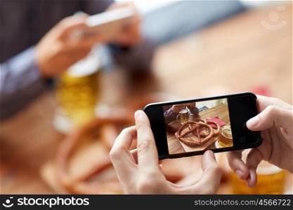 people, food, and technology concept - close up of hands with smartphone picturing beer and pretzel at bar or pub