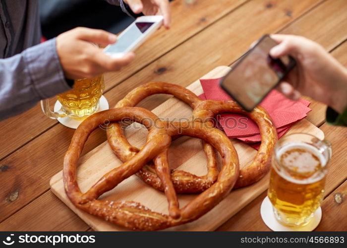 people, food, and technology concept - close up of hands with smartphone picturing beer and pretzel at bar or pub