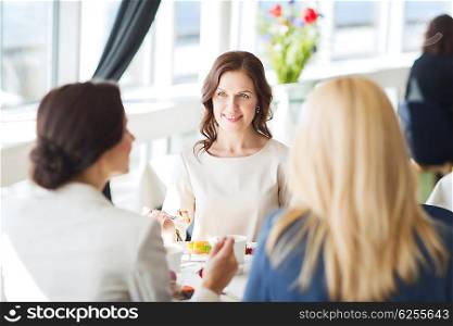 people, food, communication and lifestyle concept - happy women eating dessert and talking at restaurant