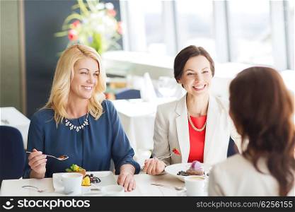 people, food, communication and lifestyle concept - happy women eating dessert and talking at restaurant