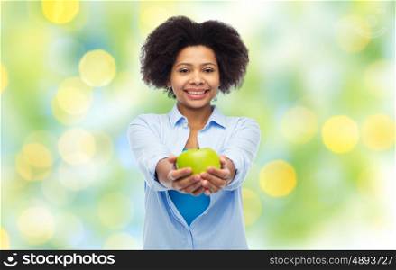 people, food, healthy eating and dental care concept - happy african american young woman with green apple over summer lights background