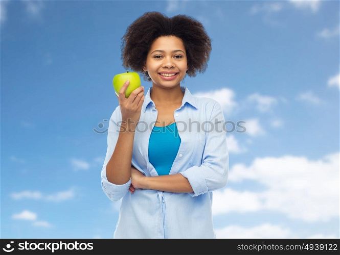 people, food, healthy eating and dental care concept - happy african american young woman with green apple over blue sky and clouds background. happy african american woman with green apple