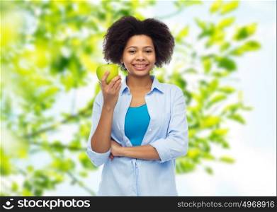 people, food, healthy eating and dental care concept - happy african american young woman with green apple over natural background. happy african american woman with green apple