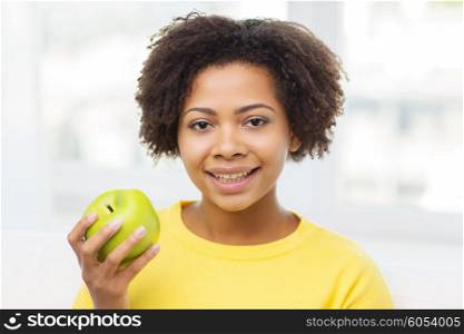 people, food, healthy eating and dental care concept - happy african american young woman with green apple at home