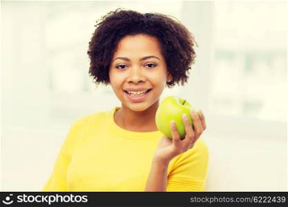 people, food, healthy eating and dental care concept - happy african american young woman with green apple at home