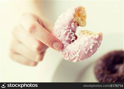 people, food, junk-food and eating concept - close up of female hand holding bitten glazed donut