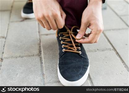 people, footwear and fashion concept - close up of male hands tying shoe laces on street