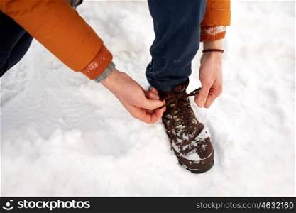 people, footwear and season concept - close up of man tying boot shoelaces outdoors in winter