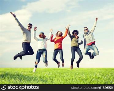 people, freedom, happiness and teenage concept - group of happy friends in sunglasses jumping high over blue sky and grass background