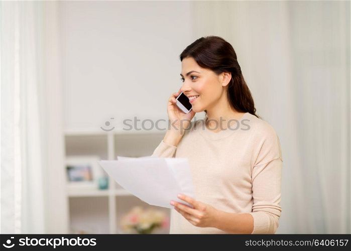 people, freelance and education concept - happy smiling woman with papers on smartphone calling at home. woman with papers calling on smartphone at home
