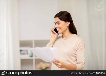 people, freelance and education concept - happy smiling woman with papers on smartphone calling at home. woman with papers calling on smartphone at home