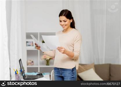 people, freelance and education concept - happy woman with papers and laptop working or learning at home. woman with papers working or learning at home. woman with papers working or learning at home