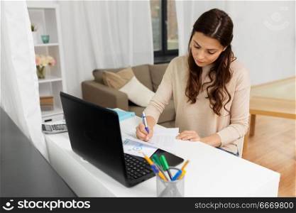 people, freelance and education concept - woman with papers and laptop computer working or learning at home. woman with papers and laptop working at home. woman with papers and laptop working at home
