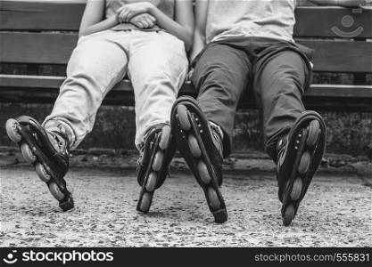 People friends in training suit with roller skates. Woman and man relaxing on bench outdoor.. People friends relaxing with roller skates.