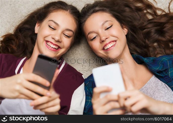 people, friends, teens and friendship concept - happy smiling pretty teenage girls lying on floor with smartphones
