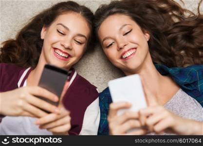 people, friends, teens and friendship concept - happy smiling pretty teenage girls lying on floor with smartphones
