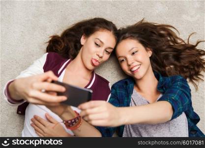 people, friends, teens and friendship concept - happy smiling pretty teenage girls lying on floor and taking selfie with smartphone. happy teenage girls on floor and taking selfie
