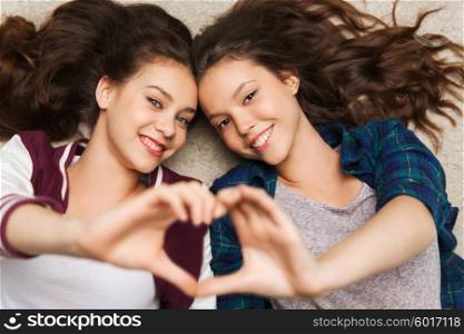 people, friends, teens and friendship concept - happy smiling pretty teenage girls lying on floor showing heart sing