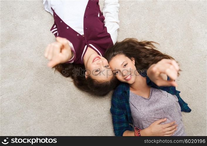 people, friends, teens and friendship concept - happy smiling pretty teenage girls lying on floor and pointing finger to you