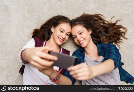 people, friends, teens and friendship concept - happy smiling pretty teenage girls lying on floor and taking selfie with smartphone