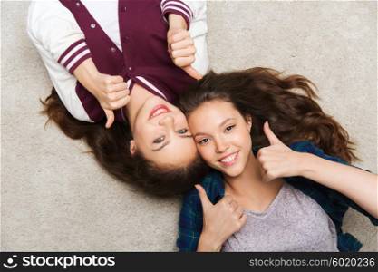 people, friends, teens and friendship concept - happy smiling pretty teenage girls lying on floor and showing thumbs up