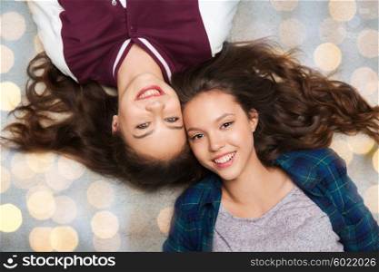 people, friends, teens and friendship concept - happy smiling pretty teenage girls lying on floor over holidays lights background