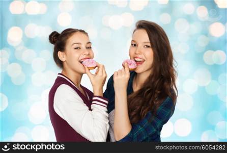people, friends, teens and friendship concept - happy smiling pretty teenage girls with donuts eating and having fun over blue holidays lights background