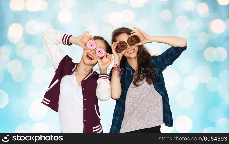 people, friends, teens and friendship concept - happy smiling pretty teenage girls with donuts making faces and having fun over blue holidays lights background