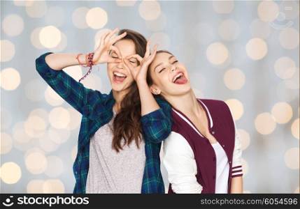 people, friends, teens and friendship concept - happy smiling pretty teenage girls having fun and making faces over holidays lights background