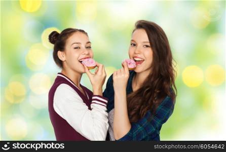 people, friends, teens and friendship concept - happy smiling pretty teenage girls with donuts eating and having fun over green holidays lights background