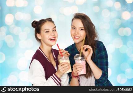 people, friends, teens and friendship concept - happy smiling pretty teenage girls drinking milk shakes and with straw over blue holidays lights background