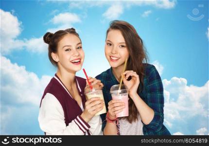 people, friends, teens and friendship concept - happy smiling pretty teenage girls drinking milk shakes and with straw over blue sky and clouds background